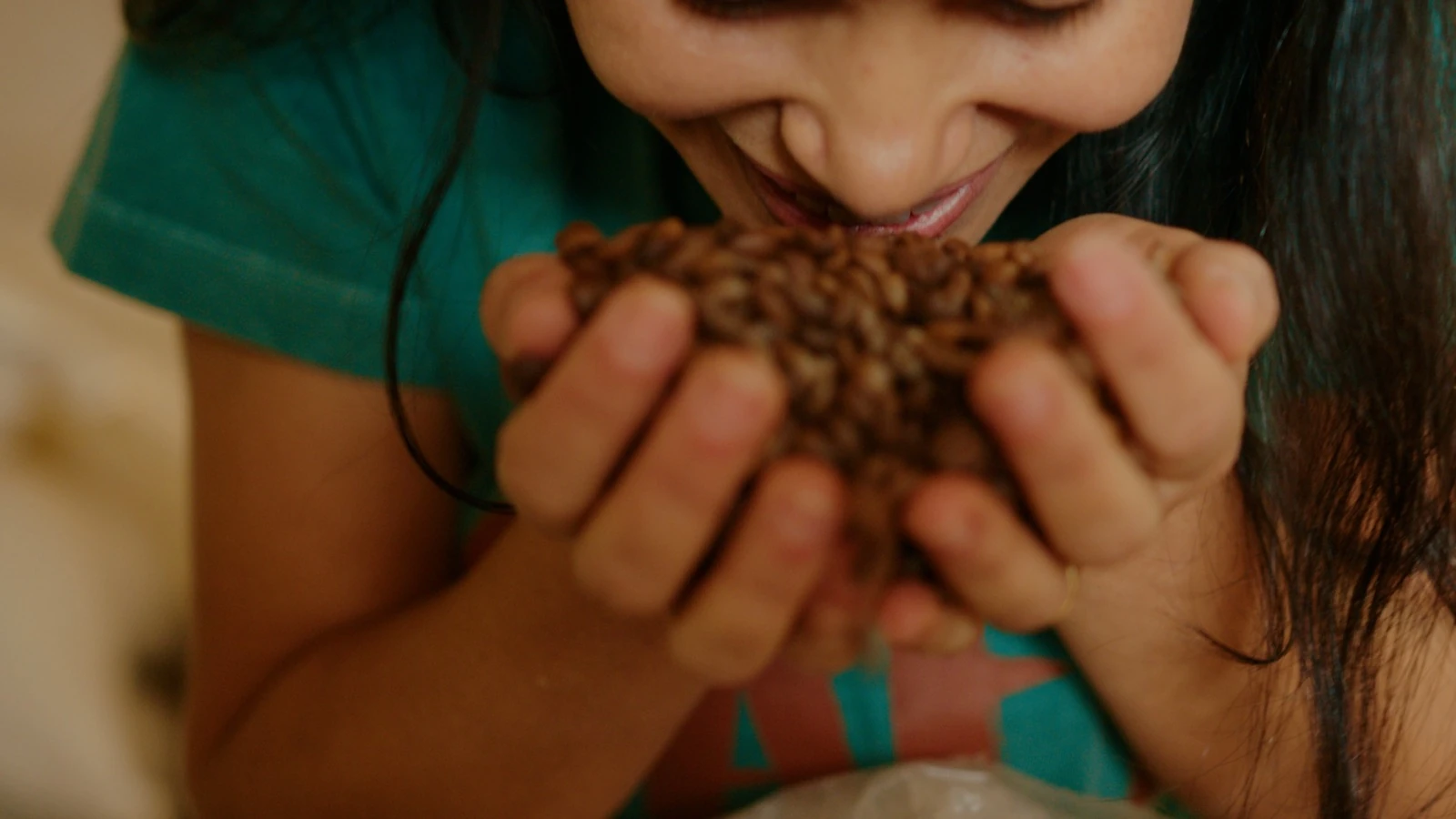 Mãos em concha segurando grãos de café torrados perto do rosto, sentindo o aroma
